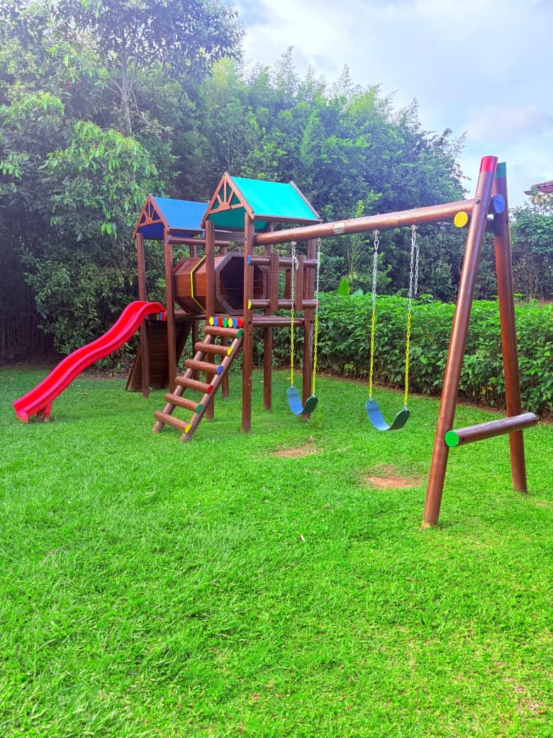 Parque infantil con tobogán rojo, columpios y casita de madera